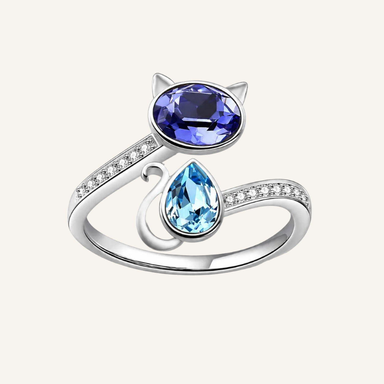 A silver cat-shaped ring featuring a large oval dark blue gemstone on the forehead and a smaller teardrop-shaped light blue gemstone on the tail, with small clear stones along the band, set against a plain white background.