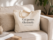 A cream canvas tote bag with black text reading 'Cat person. Obviously.