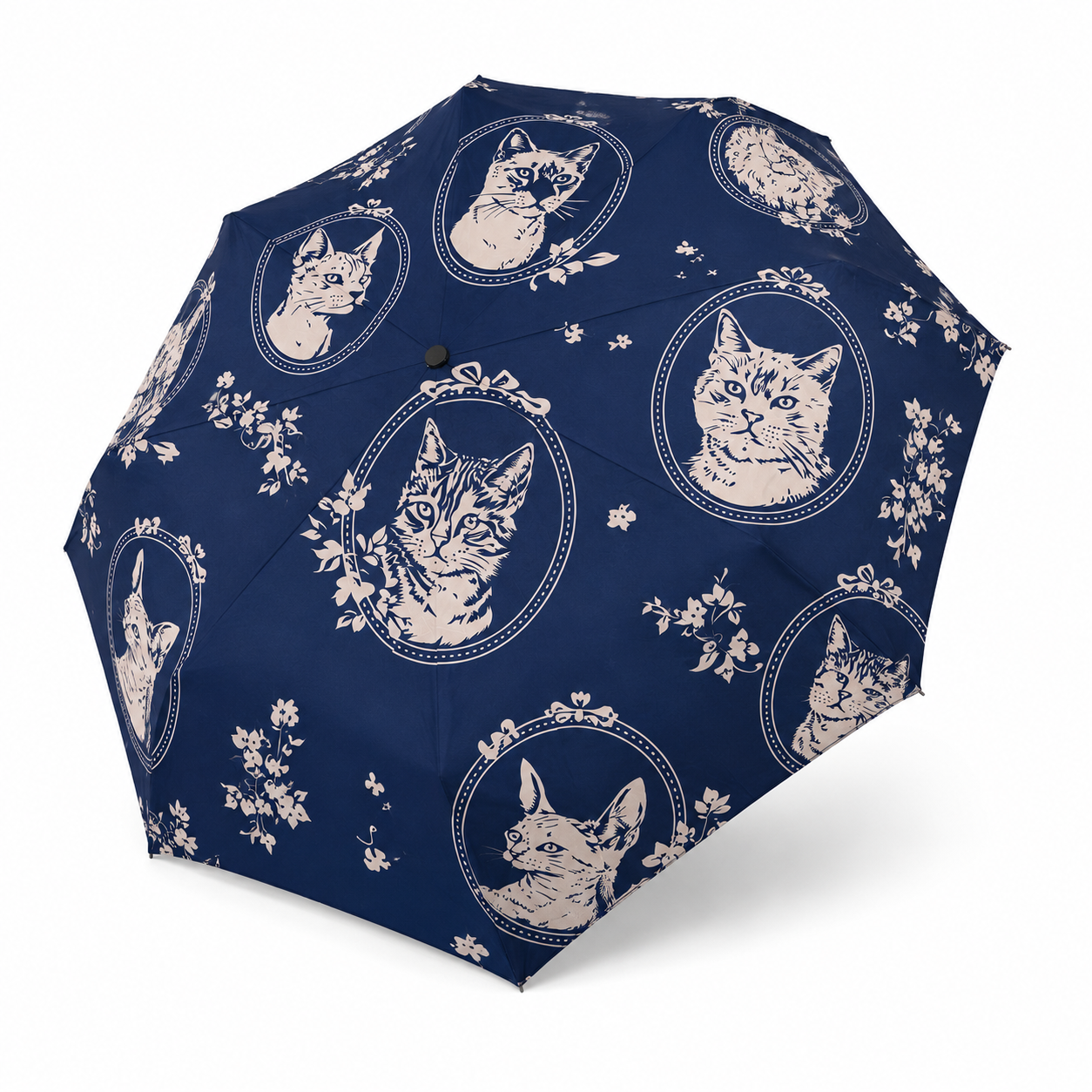 A navy blue folding umbrella with a repeating pattern of white cat portraits in oval frames and small floral motifs, shown open against a plain white background.