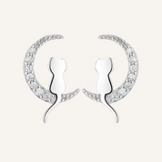 A pair of silver crescent moon stud earrings featuring a stylized cat silhouette in the center, set with small clear stones along the outer curve, on a plain white background.