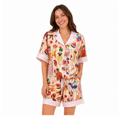 A woman modeling a two-piece pajama set featuring a colorful fruit and vegetable print on a light beige background, with light pink trim on the collar, sleeve cuffs, and shorts.