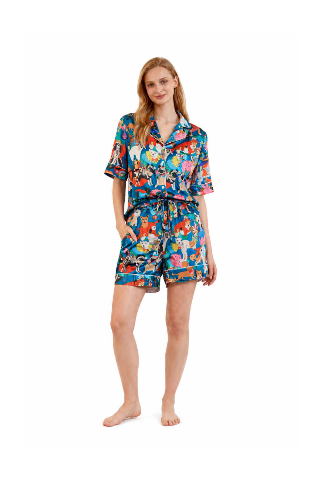 A woman modeling a short-sleeve button-front pajama shirt and matching shorts set with a colorful cartoon print, photographed against a plain white studio background.