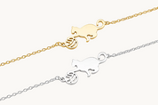 Two delicate chain bracelets shown on a white background: one in yellow gold with a cat and ball motif, and one in silver with the same cat and ball motif.