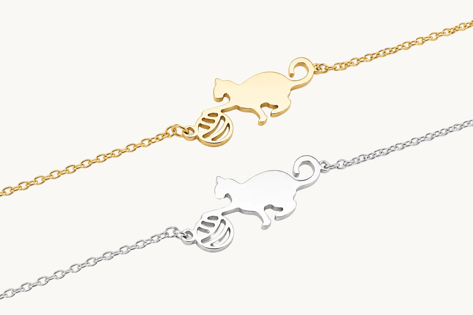 Two delicate chain bracelets shown on a white background: one in yellow gold with a cat and ball motif, and one in silver with the same cat and ball motif.