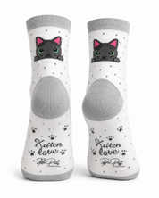 A pair of white crew socks with gray heels, toes, and cuffs, featuring a cute cartoon black kitten with pink ears peeking out, small black paw prints, and the text 'Kitten love Peter Pet' on the soles.