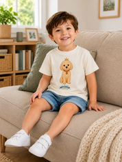 A young boy stands in a child's bedroom wearing a white t-shirt with a cartoon dog graphic and the brand name 'Whiskers' printed below it, paired with light blue denim shorts and white shoes.
