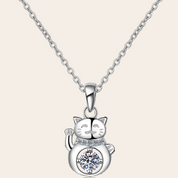 A silver-toned necklace featuring a cat-shaped pendant with a raised paw and a clear round gemstone set on its belly, shown against a light beige background.