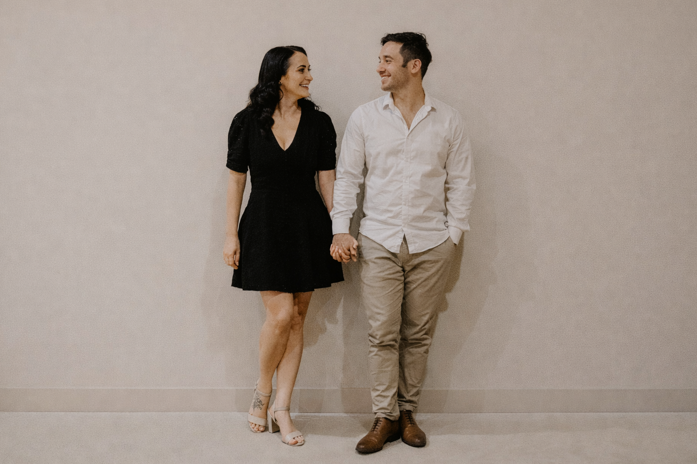 Man and woman standing side by side against a plain wall.