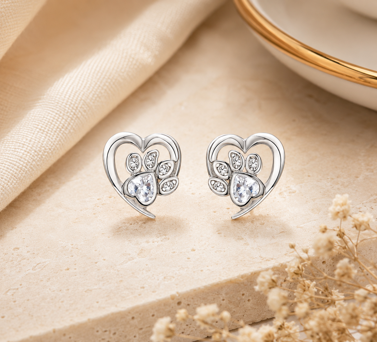 Silver heart-shaped earrings with clear stones on a beige fabric background