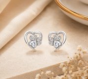 Silver heart-shaped earrings with clear stones on a beige fabric background