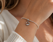 A close-up of a person's wrist wearing a delicate silver snake bracelet with a small circular charm featuring a star and crescent moon design.