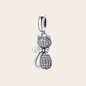 A silver cat-shaped charm pendant adorned with small clear pavé stones, featuring a silver bow and a polished silver bail at the top, shown on a white background with a soft reflection below.