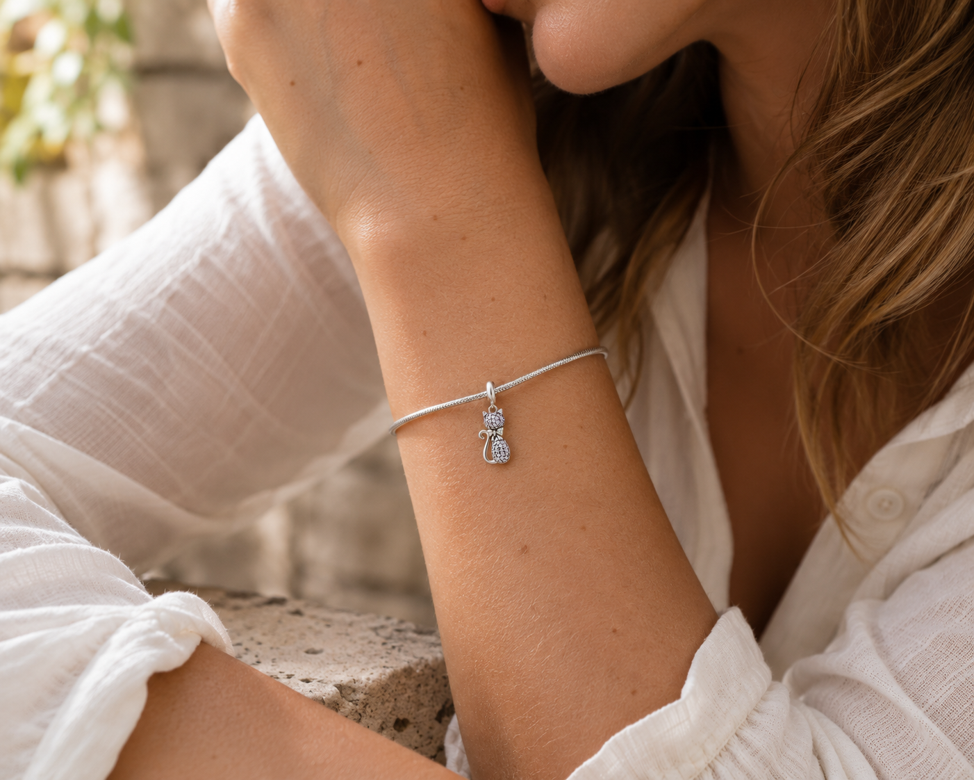 A close-up lifestyle shot of a woman wearing a delicate silver snake charm bracelet on her wrist, wearing a white blouse.