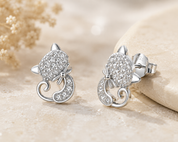Silver cat-shaped earrings with sparkling details on a beige background