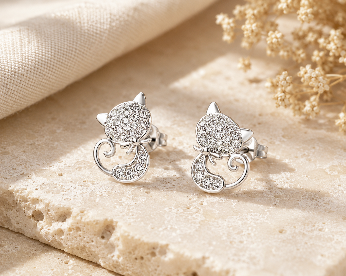 Silver cat-shaped earrings with sparkling details on a beige fabric background
