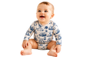 A smiling baby sitting on a white background, wearing a long-sleeve cream-colored bodysuit with a blue cartoon animal print.
