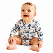 A smiling baby sitting on a white background, wearing a long-sleeve cream-colored bodysuit with a blue cartoon animal print.