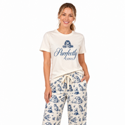 A woman modeling a two-piece pajama set consisting of an off-white t-shirt with a navy blue graphic print and matching wide-leg pants with a navy blue toile-style pattern, against a plain white background.