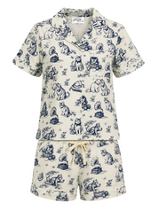 A two-piece short-sleeve pajama set featuring a matching button-up top and shorts in cream with a navy blue toile de Jouy print of dogs and cats, complete with a cream drawstring tie at the waist.
