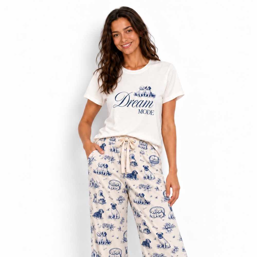 A woman modeling a matching sleepwear set consisting of a white graphic t-shirt and white wide-leg pajama pants with a blue cartoon print, set against a plain white background.