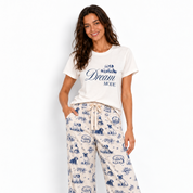 A woman modeling a matching sleepwear set consisting of a white graphic t-shirt and white wide-leg pajama pants with a blue cartoon print, set against a plain white background.