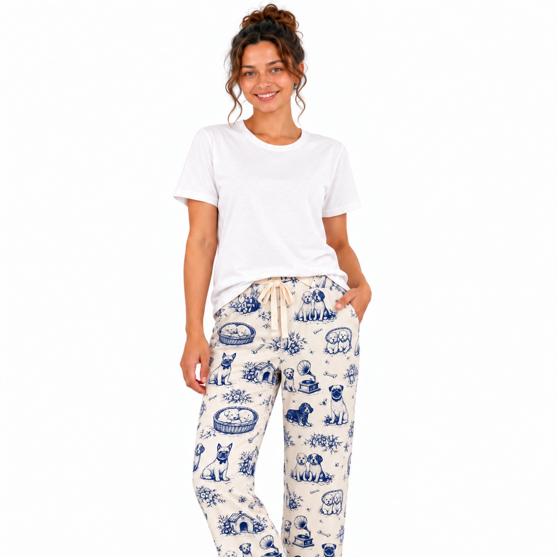 A woman modeling a matching short-sleeve button-up pajama shirt and drawstring pants set in an off-white fabric with a blue toile-style print of dogs and baskets, against a plain white background.