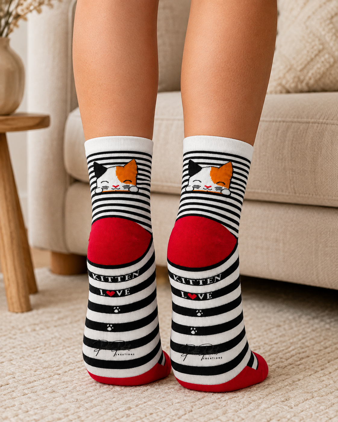A person wearing black and white striped socks with a kitten illustration and the words 'KITTEN LOVE' on the sides, photographed indoors on a carpeted floor in front of a sofa.