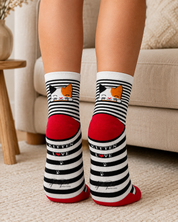 A person wearing black and white striped socks with a kitten illustration and the words 'KITTEN LOVE' on the sides, photographed indoors on a carpeted floor in front of a sofa.