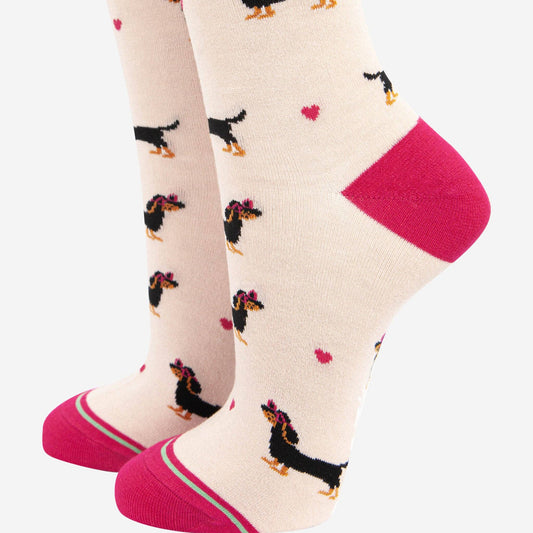 A pair of women's socks with a playful sausage dog wearing love heart sunglasses design, featuring a striped detail cuff in pink at the heel and toe.